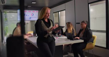 Ofis toplantısında arka planda çalışan ekip modern işyerinde liderlik ve üretkenlik gösterirken, tablet üzerinde gülümseyen kadın profesyonel inceleme notları