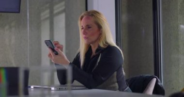 Modern ofis ortamında masa başında akıllı telefon kullanırken gülümseyen, iletişim kuran veya mesajları kontrol eden bir iş kadını