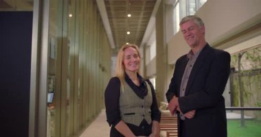 Ofis koridorunda yan yana duran gülümseyen iş adamları, kendine güvenen erkek ve kadın iş arkadaşları işyeri portresi için poz veriyorlar.