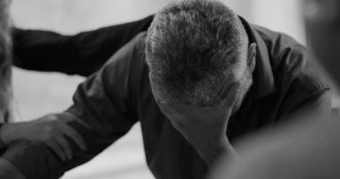 Terapi seansında ağlayan bir adam, etrafını saran destekleyici grup üyeleri derin duygusal rahatlama anında nazikçe kollarına dokunurken yüz yüze ağlar.