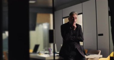 Olgun iş adamı, ofis toplantısı sırasında sessiz sedasız el pençe divan duran ve modern şirket yönetim kuruluna uzaktan bakan biri.