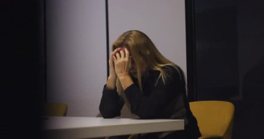 Yorgun orta yaşlı bir profesyonel modern ofisteki konferans masasında yalnız başına geçirdiği anlarda kulaklarını tıkar ve gözleri kapatır.