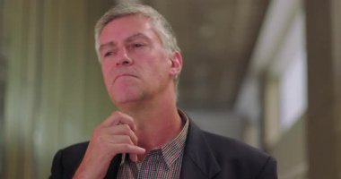 Düşünceli iş adamı ofis koridorunda düşünürken çeneye dokunuyor, modern çalışma ortamında ciddi yüz ifadesi olan olgun bir erkek profesyonel.