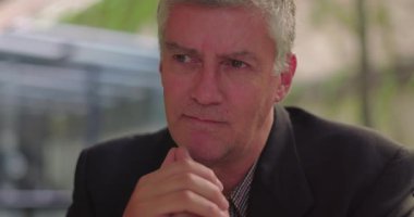 Ofis salonunda ciddi bir ifadeye sahip orta yaşlı bir adamın yakın çekimi. Duygularını sessizce işlerken elleri çeneye yakın dinleniyor.