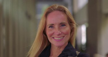 İş kadını ofis koridorundaki kameraya gülümsüyor ve saçları hafifçe havada uçuşuyor.