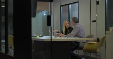 Üst düzey iş arkadaşları ofis masasında dizüstü bilgisayar ve belgelerle yüz yüze konuşarak, şirket toplantılarında iş güncellemelerini birlikte analiz ediyorlar.