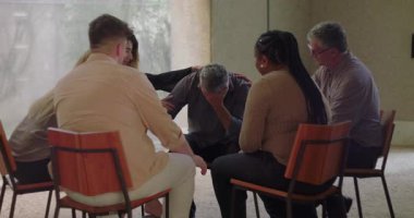 Adam grup terapisi sırasında duygusal olarak açılır. Savunmasızlığını belirtirken öne eğilir ve çemberde oturan şefkatli akranlarından destek alır.