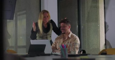 İş arkadaşları, ofis toplantısı sırasında laptopun önünde neşeli bir beşlikle başarıyı kutluyor, modern iş yerinde gülümsüyor ve birlikte duruyorlar.