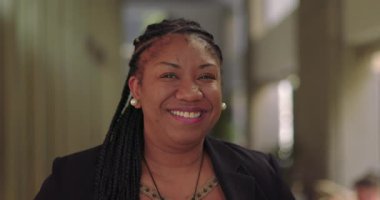 Kapalı ofis koridorunda gülümseyen Afrikalı Amerikalı kadın, rahat ve arkadaş canlısı görünüyor.