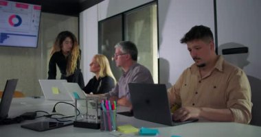 Şirket ekibi ofis sunumu sırasında dikkatle çalışır, herkes dizüstü bilgisayarlara ve veri tabloları ve iş analizlerine odaklanır.