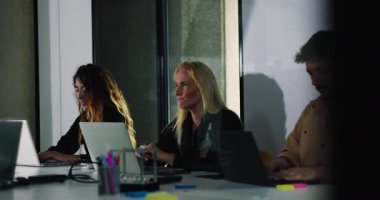 Gülümseyen erkek çalışanlar rahat ofis toplantısında dizüstü bilgisayarda çalışırken, çeşitli meslektaşlar arka planda işbirliği yapıyor.