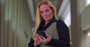 Ofis koridorunda telefonu komik bir ifadeyle kullanan iş kadını ara verdiğinde mesajları karıştırıyor.