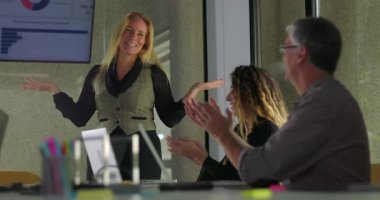 Sarışın iş kadını gülümsüyor, iltifatlarla pohpohlanıyor. Meslektaşları modern ofis konferans odasında yaptığı toplantıda sunumunu alkışlıyor.