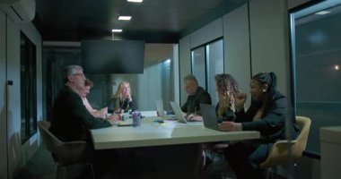 Modern yönetim kurulu masasının etrafında laptoplar ve renkli kırtasiyeler kullanarak ortak toplantılar yapan profesyonellerden oluşan bir ekip.