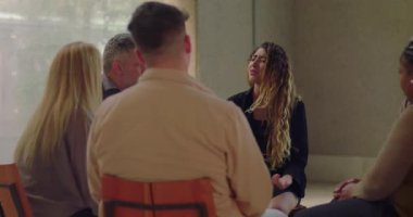 Genç bir kadın grup terapi seansında gözyaşlarıyla derin bir acı ifade ediyor. Güvenli ve şefkatli bir ortamda destekleyici akranlar tarafından çevrelenmiş.