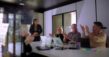 Meslektaşlar, parlak modern konferans odasında sunum sonrası sunucuları dizüstü bilgisayarlar ve dijital çizelgelerle alkışlıyorlar.