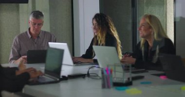 Modern ofis toplantı odasındaki dizüstü bilgisayarlar ve dijital ekran ve işbirlikçi ortamda bağımsız olarak çalışan takım