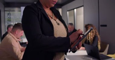 Toplantı sırasında dijital tablet kullanan Afrikalı Amerikalı iş kadınının yakın plan çekimi, modern konferans odasında işbirliği yapan ekip