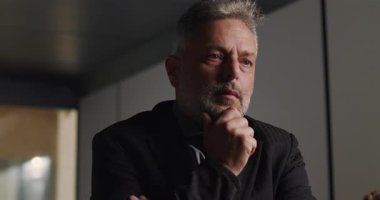 Düşünceli iş adamı, şirket toplantısında elleri çenesinde ve yoğun bakışlarıyla profesyonel yönetim kurulu ortamında kayboldu.