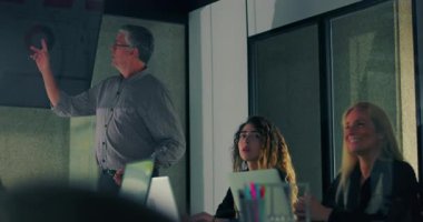 Erkek sunucu ekrandaki grafiğe işaret ederken takım dijital veri görselleştirmesi ile modern ofis toplantısında dinliyor