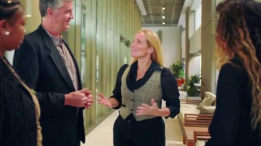 Çeşitli profesyonel gruplar koridorda dikilip işbirliği içinde konuşuyorlar. Kadın modern ofiste ifadelerle tartışmayı yönetiyor.