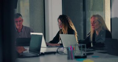 Çeşitli iş arkadaşları modern konferans odasında ofis toplantısı sırasında dizüstü bilgisayarlara yoğunlaşır, sessiz işbirliği ve profesyonel iş akışı ile meşgul olurlar.