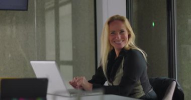 Ofiste dizüstü bilgisayarla çalışırken kamerayla göz teması kuran gülümseyen iş kadını iş günü boyunca cana yakın ve cana yakın görünüyor.