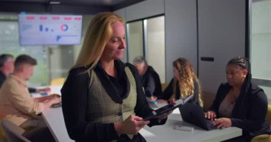 İş kadını dijital tablet kullanırken, ofis toplantısı, teknoloji odaklı üretkenlik ve profesyonel odaklı modern işyeri çalışanları arka planda işbirliği yapıyor