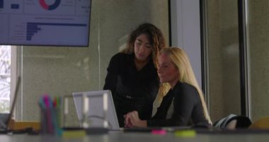 Genç iş kadını, dijital ekranla birlikte ofiste yapılan kooperatif incelemede bilgisayar ekranında sarışın meslektaşına veri gösteriyor