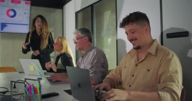 İş arkadaşları ekranda veri sunumuyla uğraşırken, gülümseyen erkek takım üyesi ofis toplantısı sırasında dizüstü bilgisayarda yazı yazıyor.