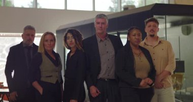 Modern ofiste, ciddi ifadeler takınan altı profesyonelden oluşan çeşitli bir grup. Parlak şirket ortamında grup portresi yapmak için birlikte poz verdiler.