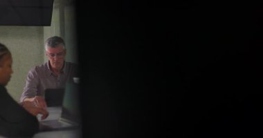 Modern çalışma ortamında masanın etrafında oturan çeşitli meslektaşlarla sessiz ofis toplantısı sırasında dizüstü bilgisayarlar üzerinde çalışan odaklanmış iş ekibi.