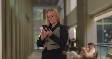 İş kadını, ofis koridorunda telefonla konuşurken, gayri resmi konuşma sırasında gülümsüyor ve yürüyordu.