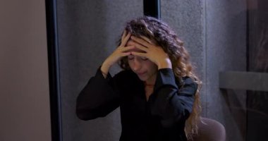 İş yerinde çalışan genç profesyonel bir kadın. Stres altında, gözleri kapalı, parmakları alnına bastırılmış, uzun bir görüşmeden sonra yorgun ve bitkin bir şekilde sandalyede oturuyor.