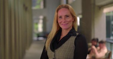 Modern bir şirket ortamında geniş ofis koridorlarında gülümseyen kendine güvenen bir iş kadını.