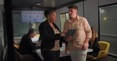 Ofis toplantısı, ekip çalışması ve analiz sırasında büyük veri ekranı önünde genç erkek meslektaşlarına tablet gösteren Afrikalı Amerikalı iş kadını