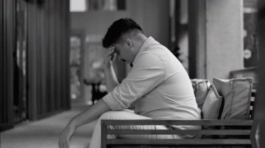 İçerideki bankta oturan genç adam, eli alnında, stresli görünüyor ve sessiz bir gerginlik ve duygusal yorgunluk anında bunalmış görünüyor.