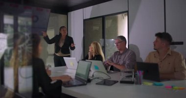 Takım toplantısında Afro-Amerikan profesyonel sunuculuk yaparken meslektaşlar da iyi aydınlatılmış kurumsal yönetim kurulunda dijital ekranı inceliyor.