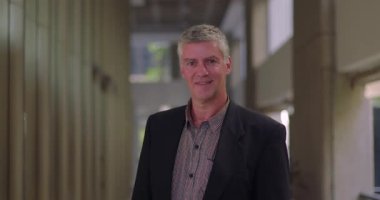 Ofis salonunda yavaşça gülümseyen, sakin ve düşünceli orta yaşlı bir adamın yakın çekimi.