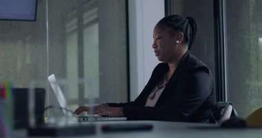 Modern kurumsal ofiste sessiz çalışma sırasında dizüstü bilgisayarda yazan odaklanmış Afrikalı Amerikalı iş kadını.