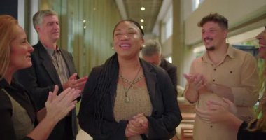 Çeşitli takımlar şirket koridorunda alkışlarken mutlu kadın gülümsüyor. Profesyoneller iş ortamında cesaret ve birlik gösteriyor.