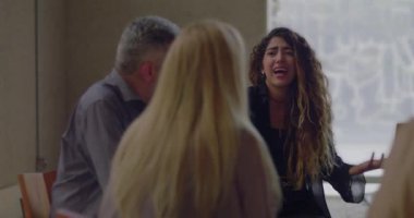 Sıkıntılı genç kadın grup terapisi sırasında acı dolu anılarını paylaştığı için ağlıyor, yaşıtları sessiz kalarak destek çemberinde şefkatli bir şekilde dinliyorlar.