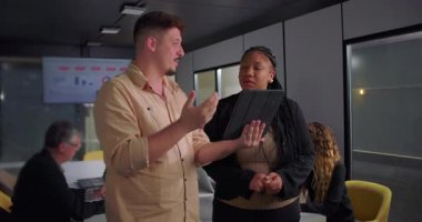 Genç bir meslektaşla dijital tablete gülümseyen Afrikalı Amerikalı iş kadını, modern ofiste takım toplantısı sırasında işbirliği anı.