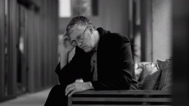 Yaşlı adam içeride oturuyor, elleri çenesinde, derin düşüncelere dalmış profesyonel ortamdaki bankta derin düşüncelere dalmış.