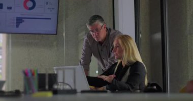 Erkek meslektaşım, bilgisayardaki verileri dijital ekranla inceleyen sarışın iş kadınına yardım etmek için eğildi.