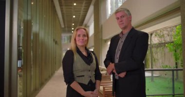 İş arkadaşları modern ofis koridorunda güvenle duruyorlar, erkek ve kadın profesyoneller iş portresi için birlikte poz veriyorlar.