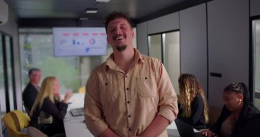 Gülümseyen genç işadamı elleri ceplerinde, kendinden emin ve rahat tavırları olan konferans masasında işbirliği yapan iş arkadaşları.