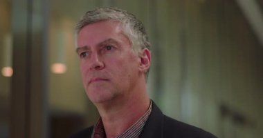 Ciddi orta yaşlı işadamı, düşünceli bir şekilde ofis koridorunda yan yan yan bakıyor, kendine güveni tam bir yönetici.