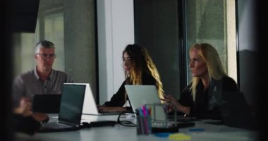 İş arkadaşları, parlak ofis ortamında gün ışığı ve modern işbirliği ortamında yapılan takım toplantısı sırasında sessizce dizüstü bilgisayar görevlerine odaklanırlar.