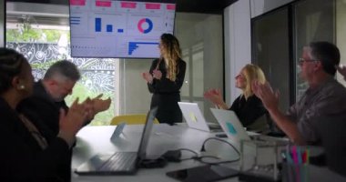 Çeşitli iş adamları, modern ofis toplantı odasındaki başarıyı kutlayan grup olarak sunulan veri sunumundan sonra bayan meslektaşlarını alkışlıyor.